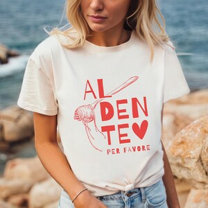 May include: A white t-shirt with a red graphic that says "AL DENTE PER FAVORE" with a drawing of spaghetti and a heart.