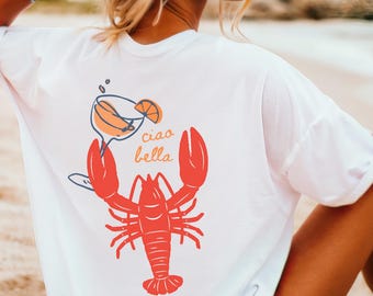 May include: White t-shirt with a red lobster holding a glass of orange juice and the text "ciao bella" printed on the back.