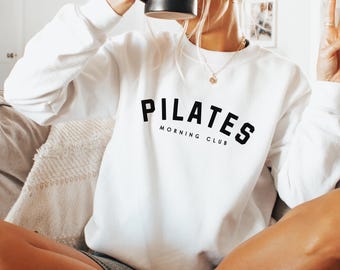 May include: White sweatshirt with black text that reads "Pilates Morning Club".