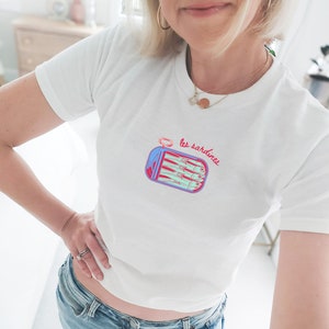 May include: White t-shirt with a graphic of a can of sardines and the text "les sardines" in red and blue.