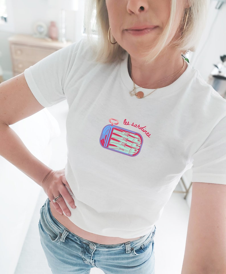 May include: White t-shirt with a graphic of a can of sardines and the text "les sardines" in red and blue.