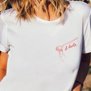 Puede incluir: Camiseta blanca con un dibujo de l&iacute;nea roja de un tenedor con espaguetis y el texto "al dente" escrito en rojo.