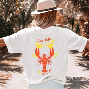 May include: White t-shirt with a red lobster holding two yellow cocktails and the text "Ciao Bella Limoncello" printed on the back.