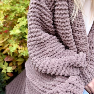 May include: A soft, mauve cardigan with a chunky knit texture. The cardigan is open in the front and has long sleeves.