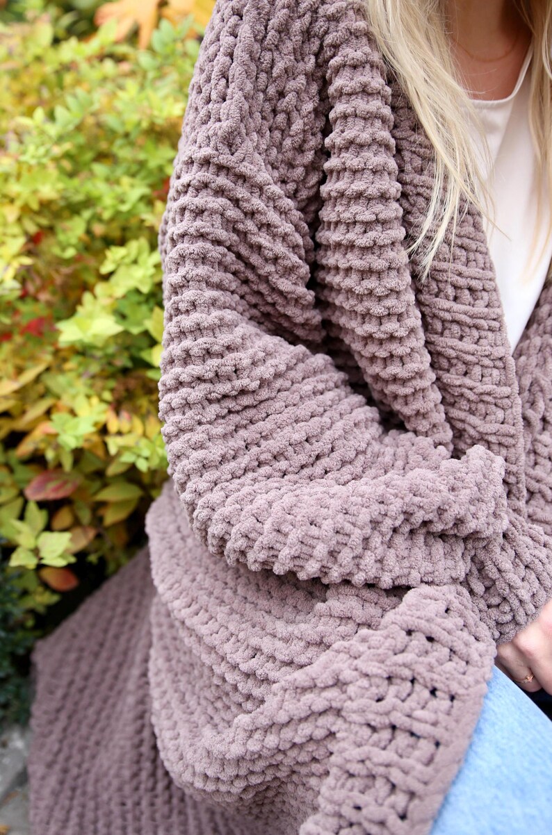 May include: A soft, mauve cardigan with a chunky knit texture. The cardigan is open in the front and has long sleeves.
