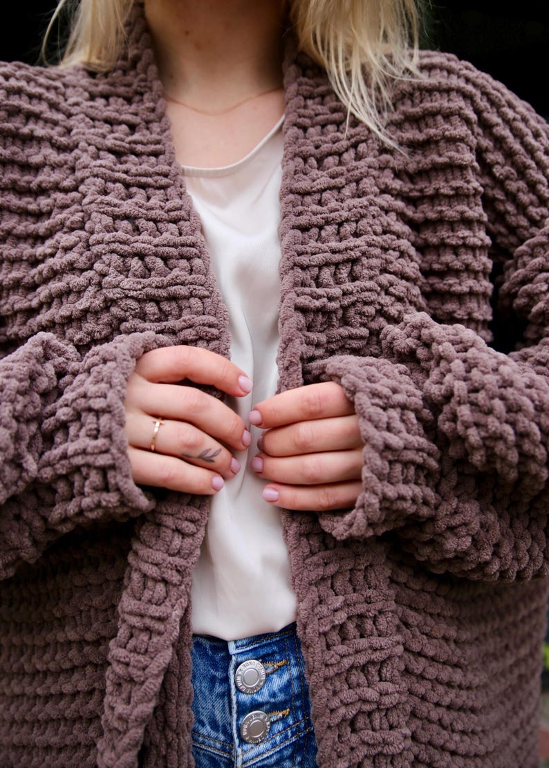 May include: A mauve knitted cardigan with a chunky knit texture. The cardigan is open in the front and has long sleeves.