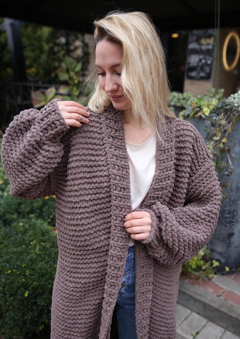 May include: A long, brown, chunky knit cardigan with a V-neck and long sleeves. The cardigan is made of a soft, fuzzy material and has a relaxed fit.