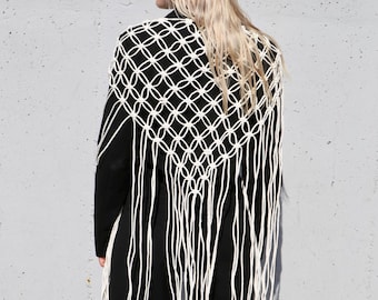 May include: A white crocheted shawl with long fringe. The shawl is worn over a black blazer and pants.