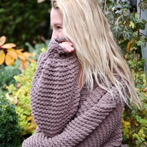 May include: A woman wearing a brown chunky knit sweater with long sleeves. The sweater is made of a soft, fuzzy yarn.