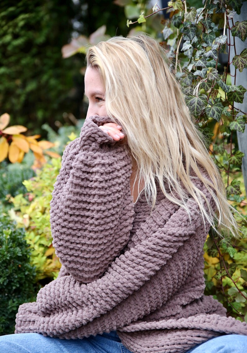 May include: A woman wearing a brown chunky knit sweater with long sleeves. The sweater is made of a soft, fuzzy yarn.