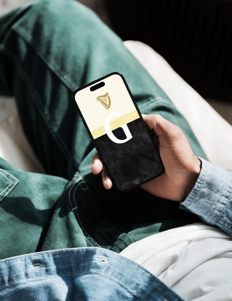 May include: A black smartphone with a white and gold case. The case has a harp logo and the letter "G" on it.