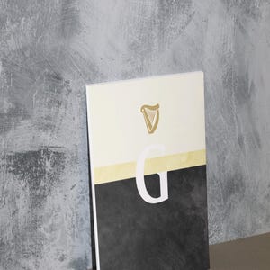 May include: A white and black poster with a gold harp logo and the letter "G" in white. The poster has a textured background.