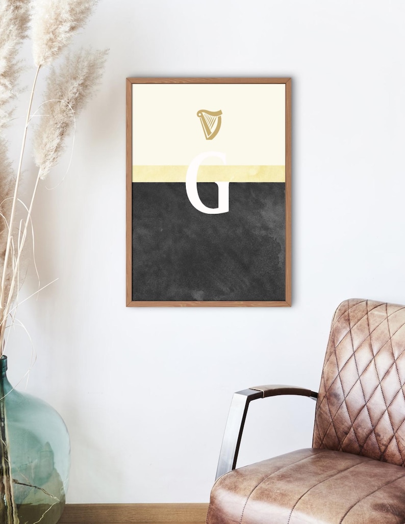 May include: A framed print with a black and white background. The top portion of the print is a light yellow color with a gold harp symbol. The bottom portion of the print is black with a white letter "G" in the center.