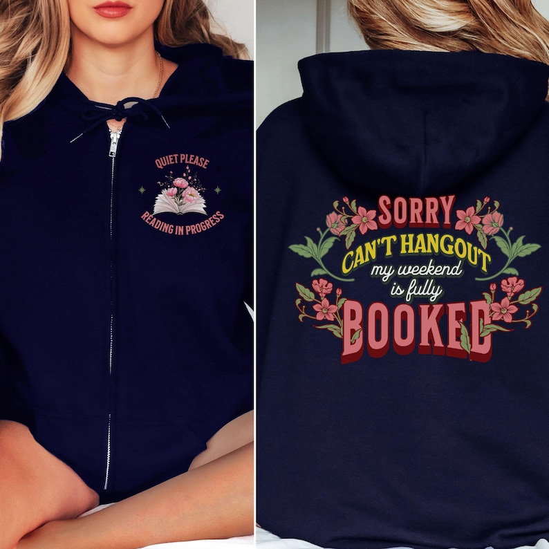 以下が含まれることがあります： ネイビーブルーのジップアップパーカー。フロントには花が描かれた開いた本と「QUIET PLEASE READING IN PROGRESS」の文字がプリントされています。バックには花柄のデザインと「SORRY CAN'T HANGOUT my weekend is fully BOOKED」の文字が施されています。