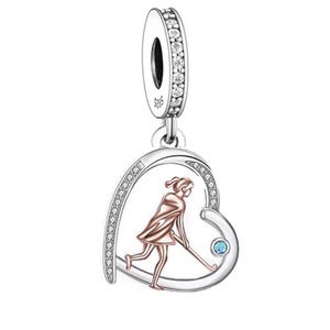 May include: Silver charm with a heart-shaped design featuring a girl playing field hockey. The charm is decorated with clear cubic zirconia stones and a blue stone.