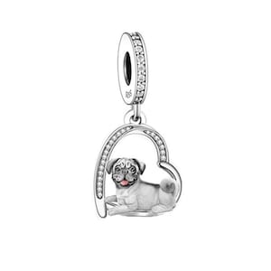 May include: Silver charm featuring a pug dog inside a heart-shaped frame with clear cubic zirconia stones. The charm has a loop at the top for attaching to a bracelet or necklace.