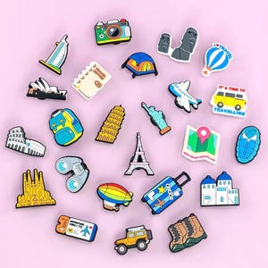 May include: A collection of colorful travel-themed charms, including a camera, Eiffel Tower, Statue of Liberty, and a map. Other charms include a backpack, airplane, and a suitcase with the word "SOOUO".