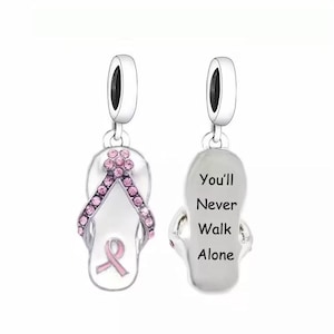 May include: Silver charm shaped like a flip-flop with pink rhinestones and a pink ribbon. The back of the charm is engraved with the words "You'll Never Walk Alone."
