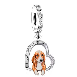 Puede incluir: Encanto de plata con un marco en forma de corazón y un perro basset dentro. El corazón tiene las palabras "Te amo para siempre" grabadas.