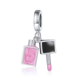 Könnte beinhalten: Silberner Anhänger mit einer rosa Nagellackflasche und einem rosa Lippenstift-Anhänger. Der Anhänger ist so konzipiert, dass er an ein Armband oder eine Halskette angebracht werden kann.