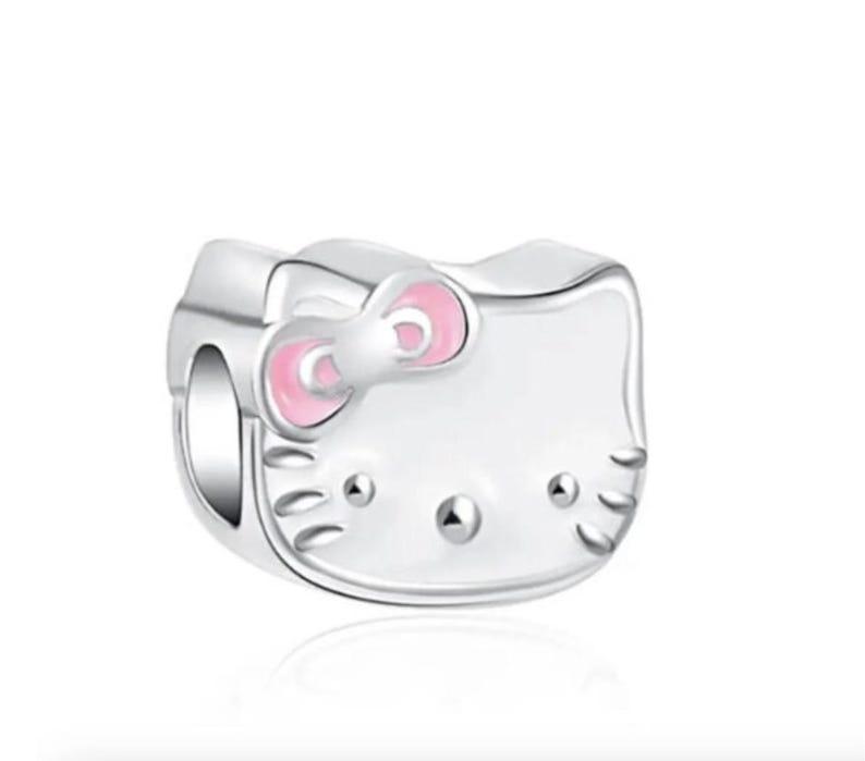 May include: A silver charm featuring a white Hello Kitty character with pink ears and a pink bow. The charm has a hole for attaching to a bracelet or necklace.