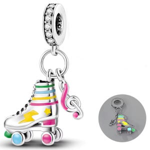 Puede incluir: Charm de plata con un patín con detalles coloridos y una clave de sol. El patín tiene un diseño de rayo amarillo y una estrella. El charm está unido a un anillo de plata con piedras transparentes.