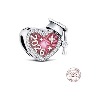 Puede incluir: Un charm de plata con forma de corazón rosa con el año "2026" y estrellas. Incluye un diseño de birrete y está adornado con cristales transparentes.