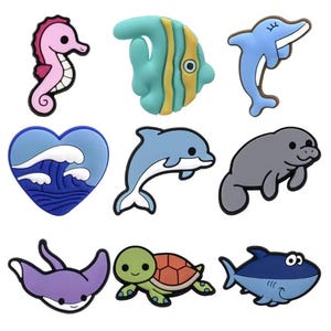 Puede incluir: Una colección de coloridos dijes de criaturas marinas, que incluyen un caballito de mar rosa, un pez turquesa y un delfín azul. Otros dijes incluyen un corazón con olas, un manatí, una raya, una tortuga y un tiburón.