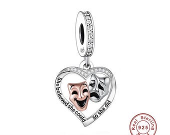 May include: Silver charm in the shape of a heart with two masks inside. The masks are a happy and a sad mask. The text around the masks reads "She believed she could so she did".