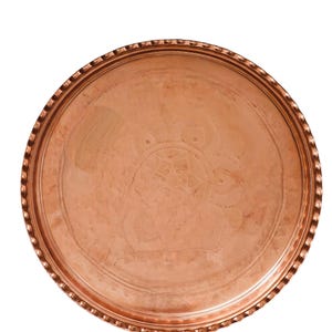 Puede incluir: Una bandeja redonda de cobre con un dise&ntilde;o en relieve en el centro. La bandeja tiene un borde decorativo y texturizado. El cobre tiene un color marr&oacute;n rojizo c&aacute;lido y un acabado pulido. La bandeja probablemente se utiliza para servir o exhibir.