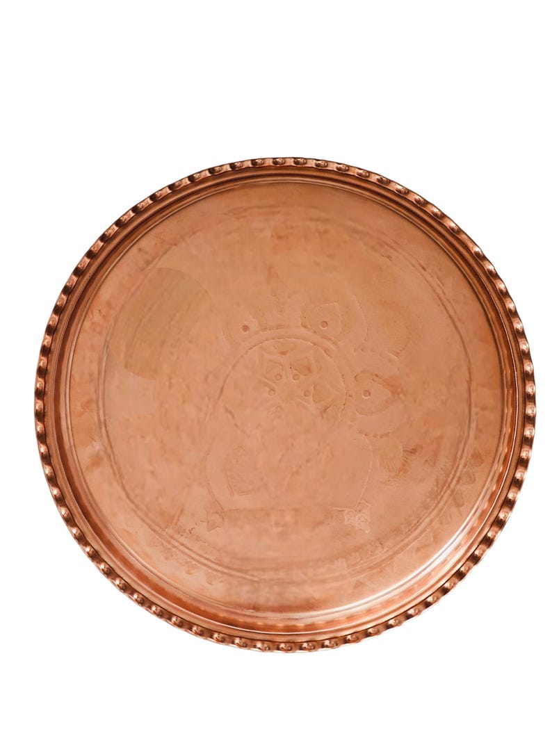 Puede incluir: Una bandeja redonda de cobre con un dise&ntilde;o en relieve en el centro. La bandeja tiene un borde decorativo y texturizado. El cobre tiene un color marr&oacute;n rojizo c&aacute;lido y un acabado pulido. La bandeja probablemente se utiliza para servir o exhibir.