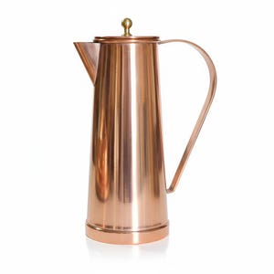 May include: A copper coffee pot with a tall, slender body and a curved handle. The pot has a lid with a small, round knob and a spout for pouring. The copper finish gives the pot a shiny, reflective appearance. The pot is likely used for brewing and serving coffee.
