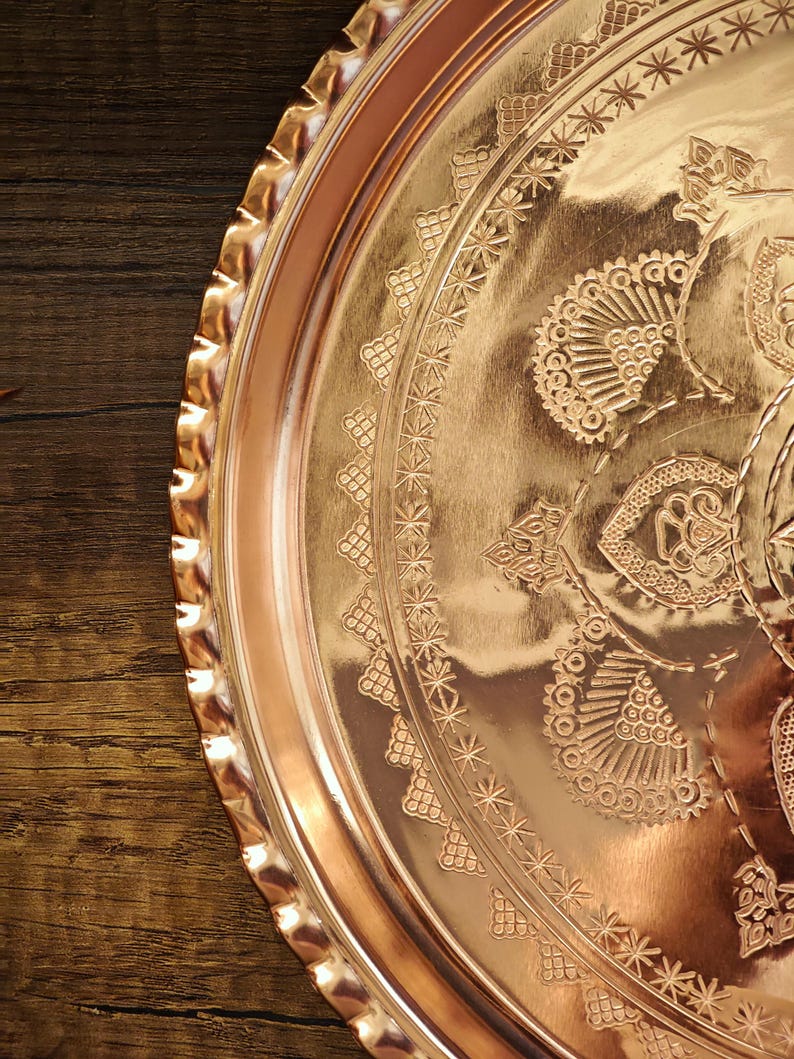 Puede incluir: Una bandeja redonda de color cobre con intrincados patrones florales y geom&eacute;tricos en relieve. La bandeja tiene un borde festoneado y un acabado pulido, que refleja la luz. El dise&ntilde;o incluye motivos detallados de estrellas y flores.