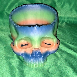 May include: A colorful skull-shaped planter with a green, blue, and orange ombre design. The planter is made of ceramic and has a smooth, glossy finish.