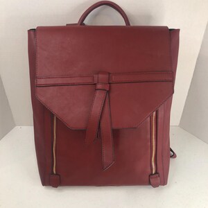 May include: A red leather backpack with a gold zipper and a bow detail on the front flap.