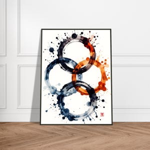May include: Abstract art print featuring four overlapping circles in shades of blue, orange, and black, with paint splatter details. The artwork is framed in a black border and set against a white background. The print is displayed on a wooden floor.