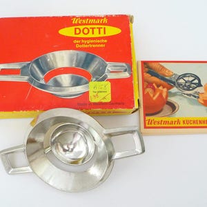 May include: A vintage Westmark Dotti egg yolk separator made of shiny metal, with a red and yellow box. The box has text in German. A small card shows the separator in use. The separator is approximately 6 inches long.