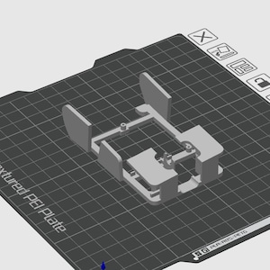 May include: A 3D printed plastic model of a small, rectangular box with a grid pattern on the top and sides. The model is printed on a textured surface.