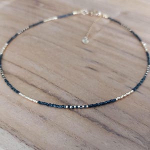 Op de afbeelding: Delicate choker ketting met kleine, afwisselend zwarte en goudkleurige kralen. De ketting heeft een fijne ketting en een verstelbare sluiting. De kralen zijn klein en gelijkmatig verdeeld, wat zorgt voor een minimalistisch en elegant ontwerp.