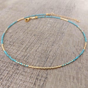 May include: A delicate gold and turquoise beaded necklace. The necklace is made of small, round beads and has a simple, elegant design.