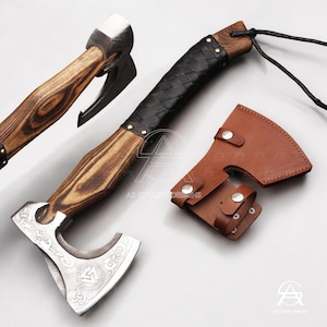May include: Axe with a wooden handle and a silver blade, featuring a black leather-wrapped grip and a brown leather sheath. The axe head has an engraved design. The handle has a wood grain pattern.