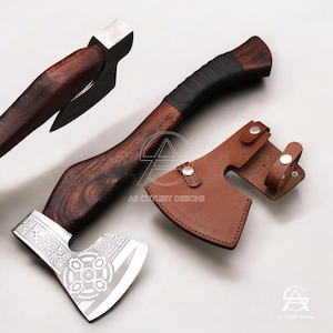 May include: Axe with a dark wooden handle and a silver blade featuring an engraved design. The handle is wrapped in black material for grip. A brown leather sheath with silver button closures is included. The axe is a handcrafted tool.