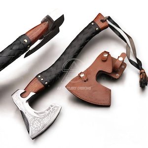 May include: A handcrafted axe with a wooden handle, a black leather-wrapped grip, and a silver-colored head with intricate engravings. Includes a brown leather sheath and a black and white lanyard with a tassel.