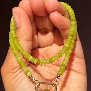 May include: A beaded necklace featuring small, round, light green beads. The necklace is secured with a gold-colored clasp. The beads are a vibrant, natural green color, and the necklace appears to be handmade.