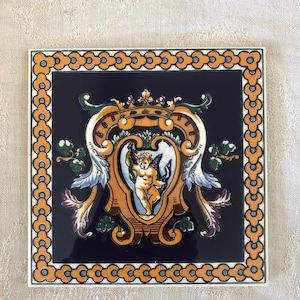 May include: A blue and gold ceramic tile with a decorative design featuring a cherub, a crown, and floral motifs. The tile is surrounded by a border of orange and blue circles.