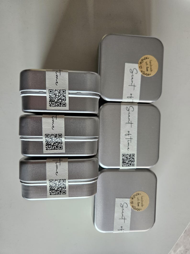 May include: A collection of small, rectangular silver tins, some with the word "Time" printed on a white label and a QR code. Other tins have a sticker that says "Scent of Time".
