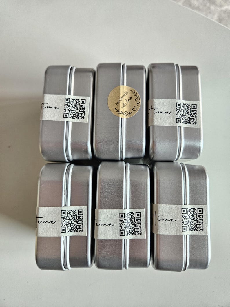 May include: Six rectangular silver metal tins with a vertical stripe down the center. Each tin has a white label with the word "time" and a QR code. One tin has a gold sticker that says "handmade with love".