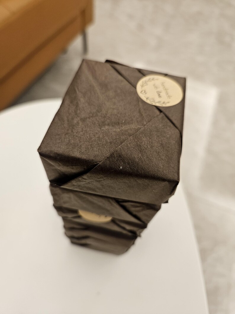 May include: A stack of three dark brown, wrapped packages. Each package is sealed with a small, round sticker that reads "handmade with love" in cursive script. The packages are stacked on a white surface.