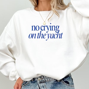 May include: White sweatshirt with the blue text "no crying on the yacht". The long-sleeved top is made of a soft material. A gold necklace is visible.