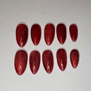 May include: A set of ten oval-shaped, red glitter press-on nails. The nails are arranged in two rows of five, with a glossy finish. The colour is a deep, vibrant red with a sparkling glitter effect.